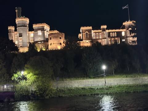 Illuminated castle buildings glowing against the night sky, reflected subtly in a nearby river.