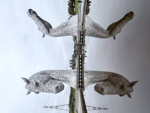 Massive steel horse head sculptures known as The Kelpies reflected perfectly in still water under a grey sky.
