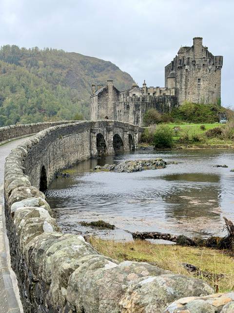 Stone arched bridge leading to Eilean Donan Castle with rippling water in the foreground.