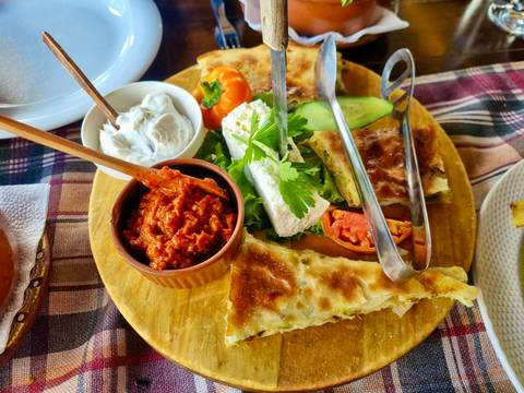 Colorful Macedonian mezze platter featuring dips, cheese, vegetables and flaky pastries on a wooden board.