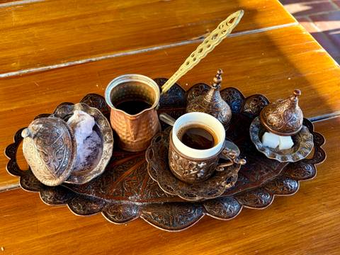 Intricately carved copper coffee set with traditional cups, pot and sugar on a decorative tray.