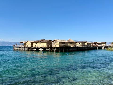 Reconstructed prehistoric stilt houses forming a wooden village over the clear blue waters of Lake Ohrid.