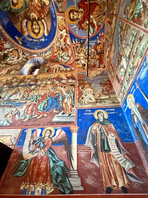 Colorful frescoes covering church walls depicting biblical scenes and saints with vivid blues and reds.