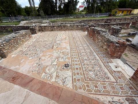 Excavated Roman mosaic floor with geometric and animal patterns surrounded by low stone walls.