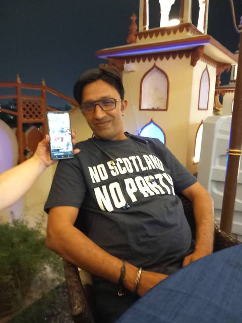 Casual portrait of a man indoors showing a smartphone picture beside him.