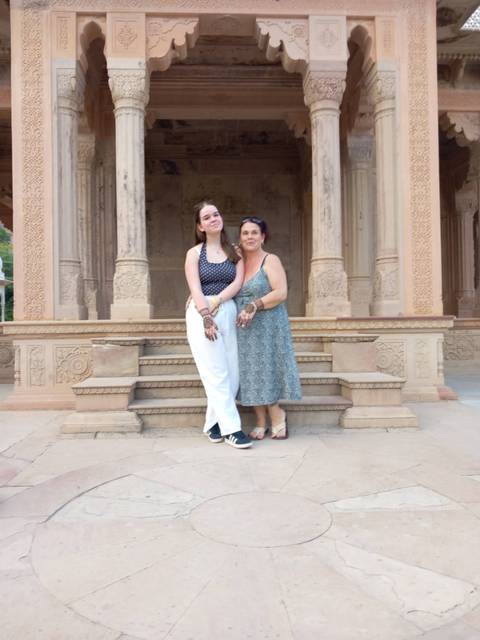Two women posing in front of intricately carved sandstone pillars.
