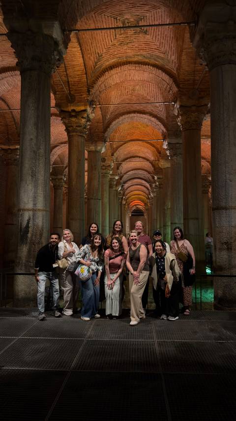 Group photo inside the dramatic arched columns of Istanbul's Basilica Cistern lit with warm tones.