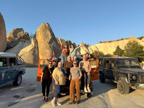 Friends pose on and around colorful jeeps amid surreal rock spires of Cappadocia at sunset.