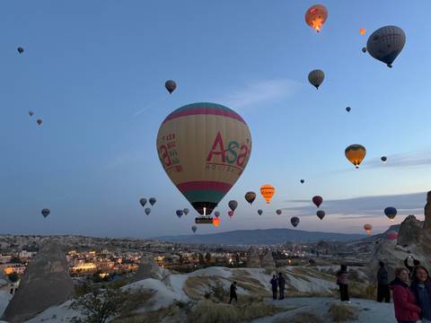 Dozens of colorful hot-air balloons rise over Cappadocia’s valleys at dawn, one prominent balloon labeled 'Asa'.