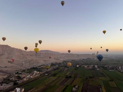 Dozens of colorful hot air balloons drift above the Nile Valley and desert cliffs at dawn near Luxor.