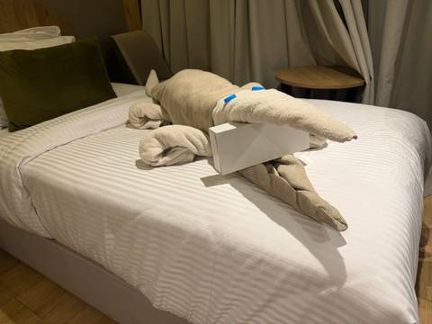 Playful towel sculpture of a crocodile on a neatly made hotel bed.