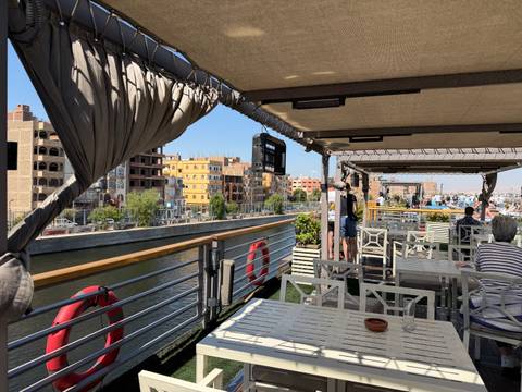 Open-air dining deck of a Nile cruise ship with passengers enjoying river views of colorful riverside buildings.