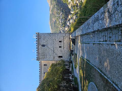 Stone castle wall and path overlook valley town under clear blue sky.