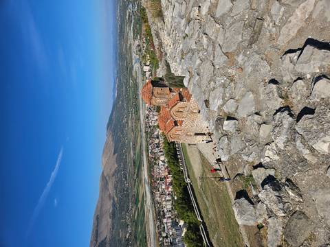 Small hillside Byzantine church overlooks broad Albanian valley with tourists nearby.