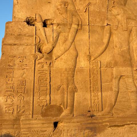 Close-up of sunlit ancient stone relief with carved figures and hieroglyphics.