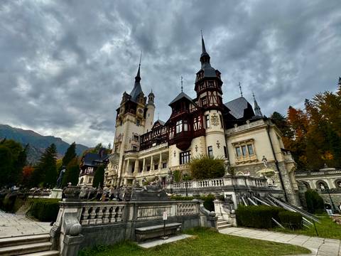 Grand Neo-Renaissance Peles Castle with ornate towers set against moody sky and mountains.