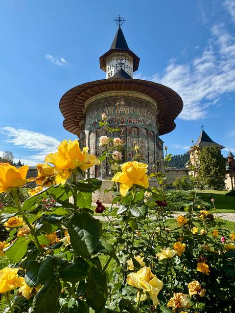 Colorful flowers framing fresco-covered exterior of Voronet painted monastery tower.