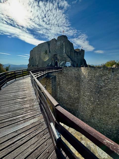 Wooden walkway leading to stone fortress gate spanning deep dry moat.