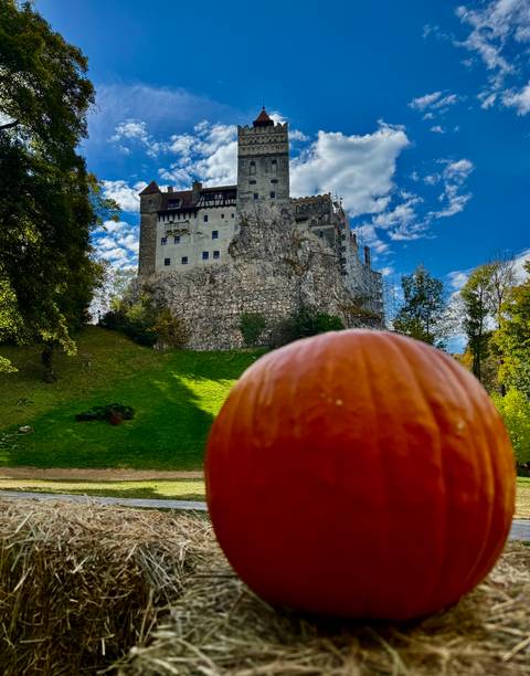 Bran Castle rising on rocky hill with large pumpkin in foreground on sunny day.