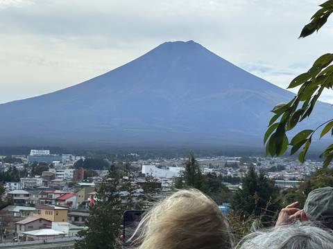 Mount Fuji dominates the skyline above a lakeside town, partially framed by a tourist’s head in the foreground.