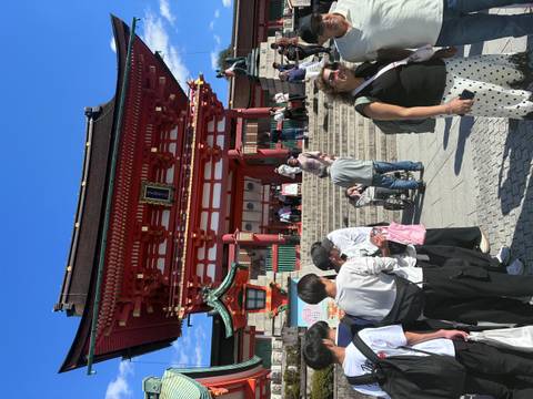 Red torii gate and main entrance of Fushimi Inari Shrine bustle with visitors under a bright blue sky.