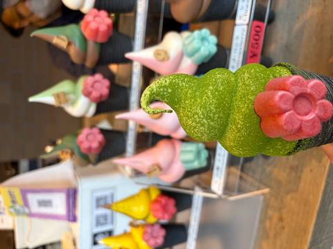 Bright green matcha soft-serve ice cream with a pink flower decoration, with colorful cones in the background.