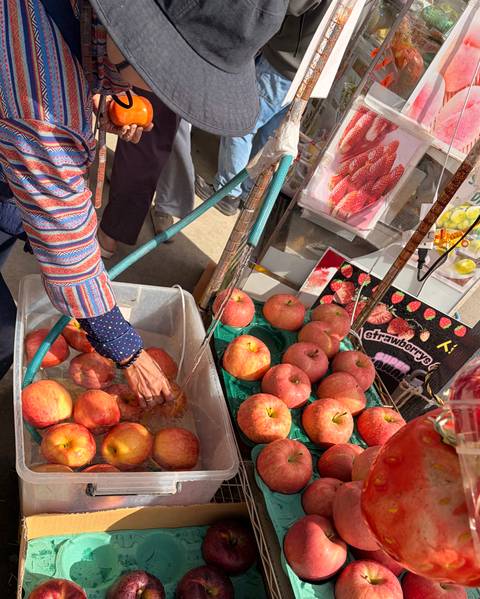 Market stall with fresh apples being washed in a plastic tub and fruit displays all around.
