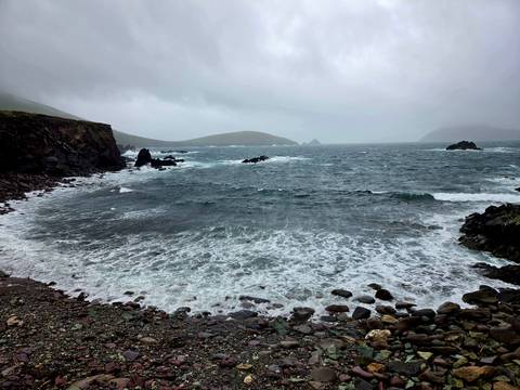 Stormy Atlantic waves crash against rugged rocky coast under misty skies on the Dingle Peninsula.