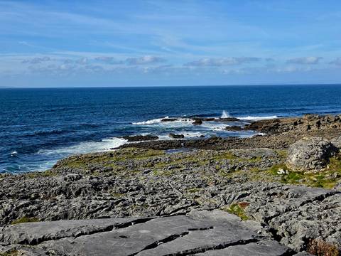 Rocky, wave-splashed Burren shoreline meets the deep blue Atlantic under clear skies.