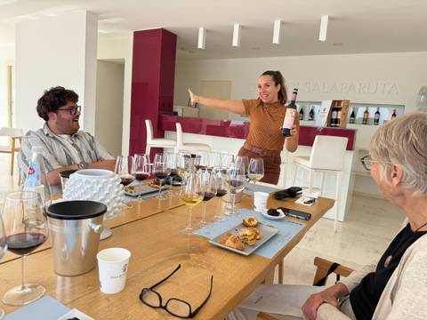 Enthusiastic sommelier showcasing a bottle during an indoor Sicilian wine tasting with glasses and snacks on the table