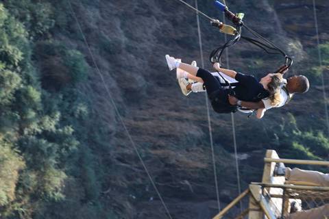 A tandem pair swinging high above a steep, green gorge on adventure cables.