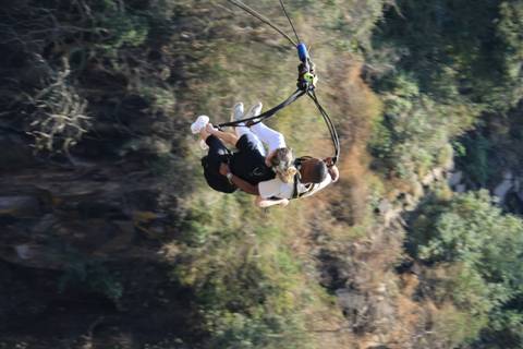 A pair mid-air above a dramatic gorge, suspended on swing ropes.
