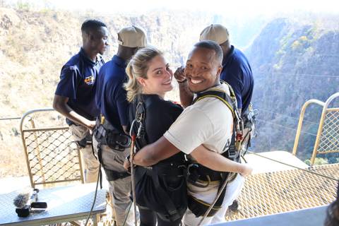 A happy couple in harnesses posing for a photo on an adventure platform with guides nearby.
