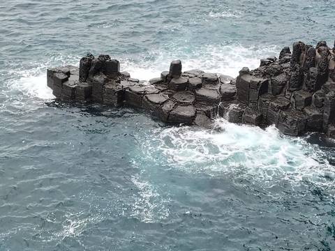 Columnar basalt rock formation surrounded by turquoise ocean waves crashing against the shore.