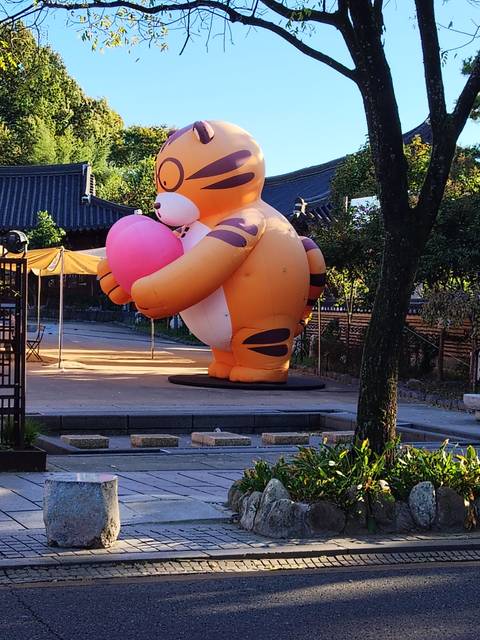 Large inflatable tiger holding a pink egg set in a courtyard of traditional Korean tile-roof buildings.