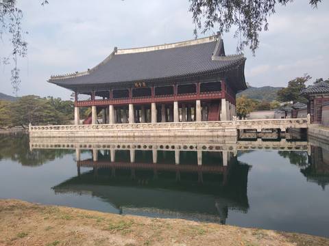 Elegant pavilion with tall columns mirrored in a still pond inside a Korean palace garden.