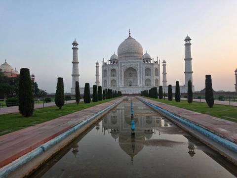 Iconic Taj Mahal and its reflecting pool at dawn with subtle pastel sky.