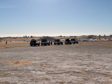 Convoy of off-road vehicles parked on the flat, sun-bleached desert plain.