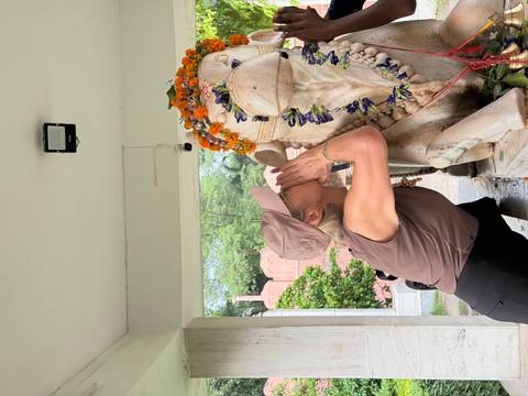 Female traveller playfully whispering into flower-adorned stone lion statue at a temple.