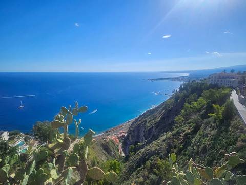 Bright Mediterranean vista with cactus in the foreground, cliffside road and sweeping sea views.
