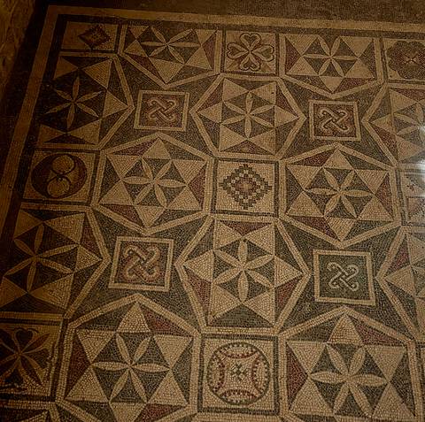 Ancient floor mosaic composed of repeating star and geometric patterns in earth tones.