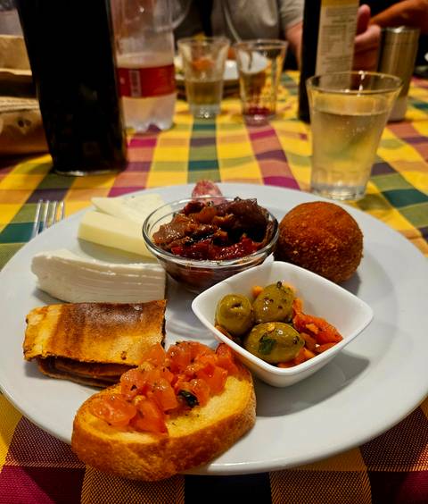 Colourful Sicilian antipasto plate with cheeses, olives, caponata and arancini on checked tablecloth.