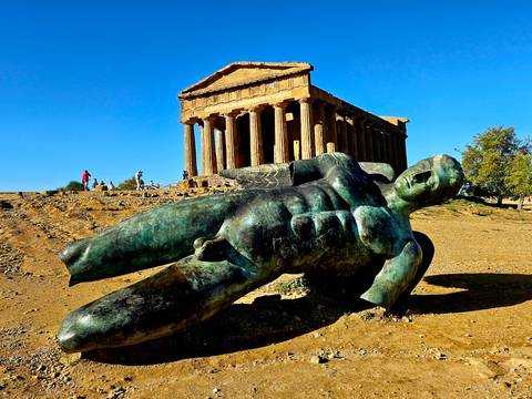 Bronze fallen Icarus statue lying before the well-preserved Temple of Concordia at the Valley of the Temples on a sunny day.