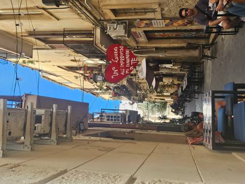 Charming narrow alley with outdoor tables, balconies full of flowers and a heart-shaped sign with Italian love phrase.