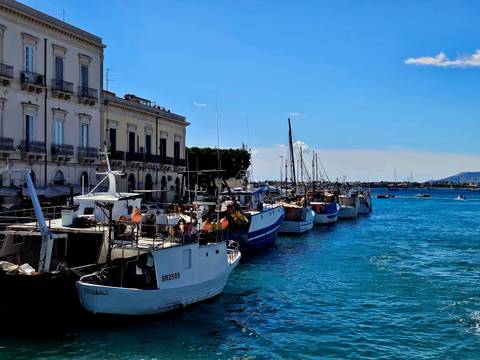 Row of small fishing boats moored along the waterfront promenade of a historic coastal city.
