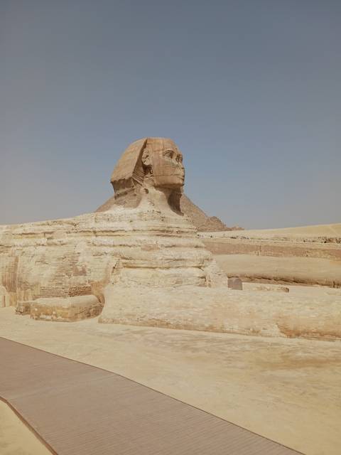 Daytime side view of the Great Sphinx and desert plateau under hazy sky.