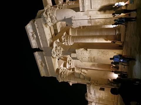 Impressive lit columns and capitals of Kom Ombo Temple at night with visitors exploring.