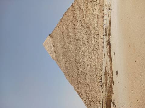 Full view of the Great Pyramid of Giza rising against a pale desert sky.