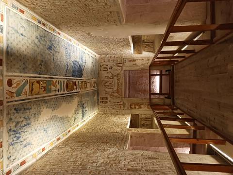 Tomb chamber with blue star-patterned ceiling and intricate wall reliefs illuminated by soft lighting.