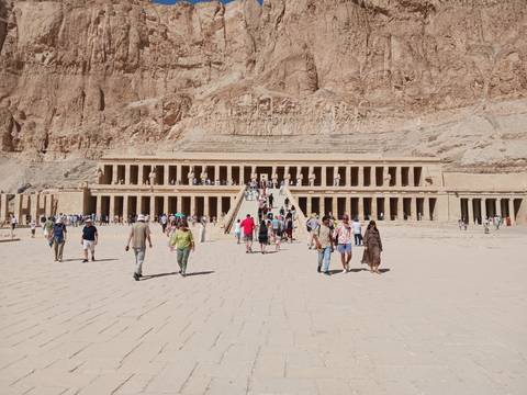 Wide courtyard view of the terraced Temple of Hatshepsut set against rugged cliffs with tourists approaching.